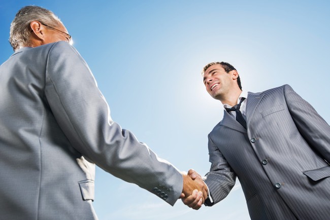 Businesspeople shaking hands against the sky.
